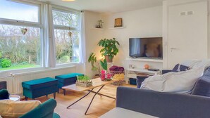 A modern living room with a large window, a flat-screen TV, and a variety of seating options including a sofa and chairs.