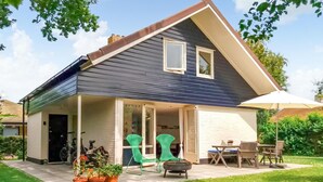 A two-story house with a covered patio, green chairs, and a table.
