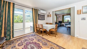 Ein Zimmer mit Esstisch, Stühlen, einem gemusterten Teppich und Blick auf eine Berglandschaft durch ein großes Fenster.