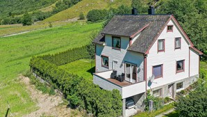 Ein zweistöckiges Haus mit Balkon, umgeben von üppigen grünen Feldern und einer hügeligen Landschaft.