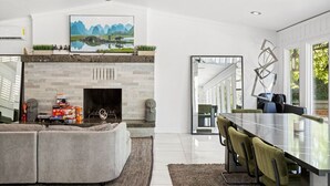 Una sala de estar moderna con chimenea, un comedor con mesa de vidrio y un cuadro grande sobre la chimenea.