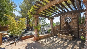 Un patio cubierto con suelo de piedra, una pérgola, una estatua de Buda y un reloj en la pared.