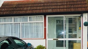 A two-story house with a brown tiled roof, white exterior walls, and two windows with white curtains. - Clean & Cosy 3 Bed House with Free Pvt Parking (Croydon)