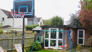 A backyard with a basketball hoop, a swing set, a wooden playhouse, and a garden. - Clean & Cosy 3 Bed House with Free Pvt Parking (Croydon)