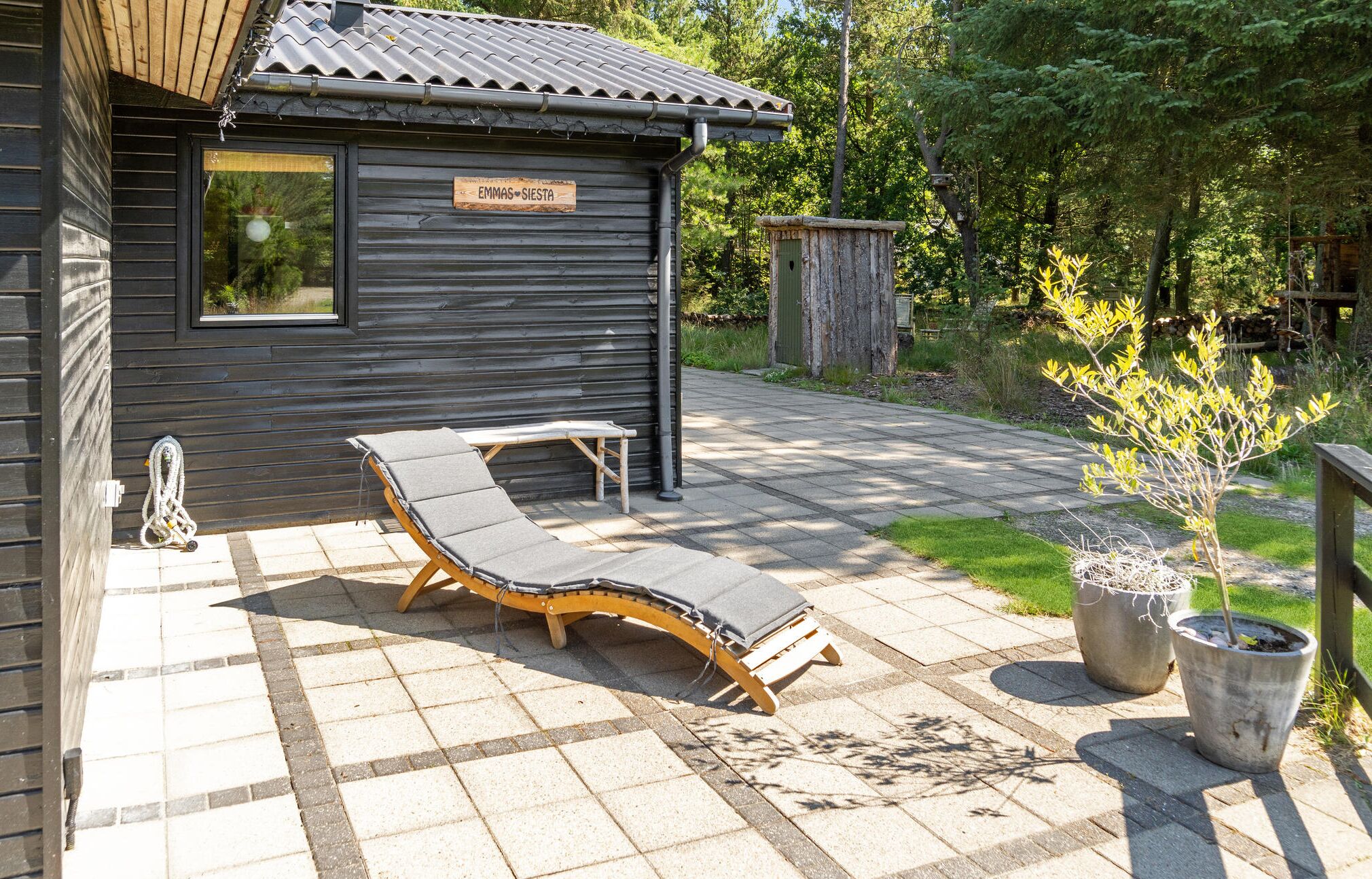 A wooden cabin with a sign reading "EMMAS SIESTA" and two lounge chairs on a paved patio.