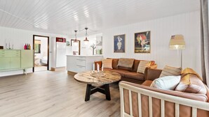 Ein geräumiges Wohnzimmer mit einem runden Holztisch, einem braunen Ledersofa mit Kissen, einem weißen Schrank und einem weißen Kühlschrank.