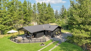 Eine Lodge mit überdachter Terrasse, Sitzgelegenheiten im Freien und Blick auf den umliegenden Wald.