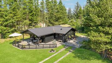 A lodge with a covered patio, outdoor seating, and a view of the surrounding forest.