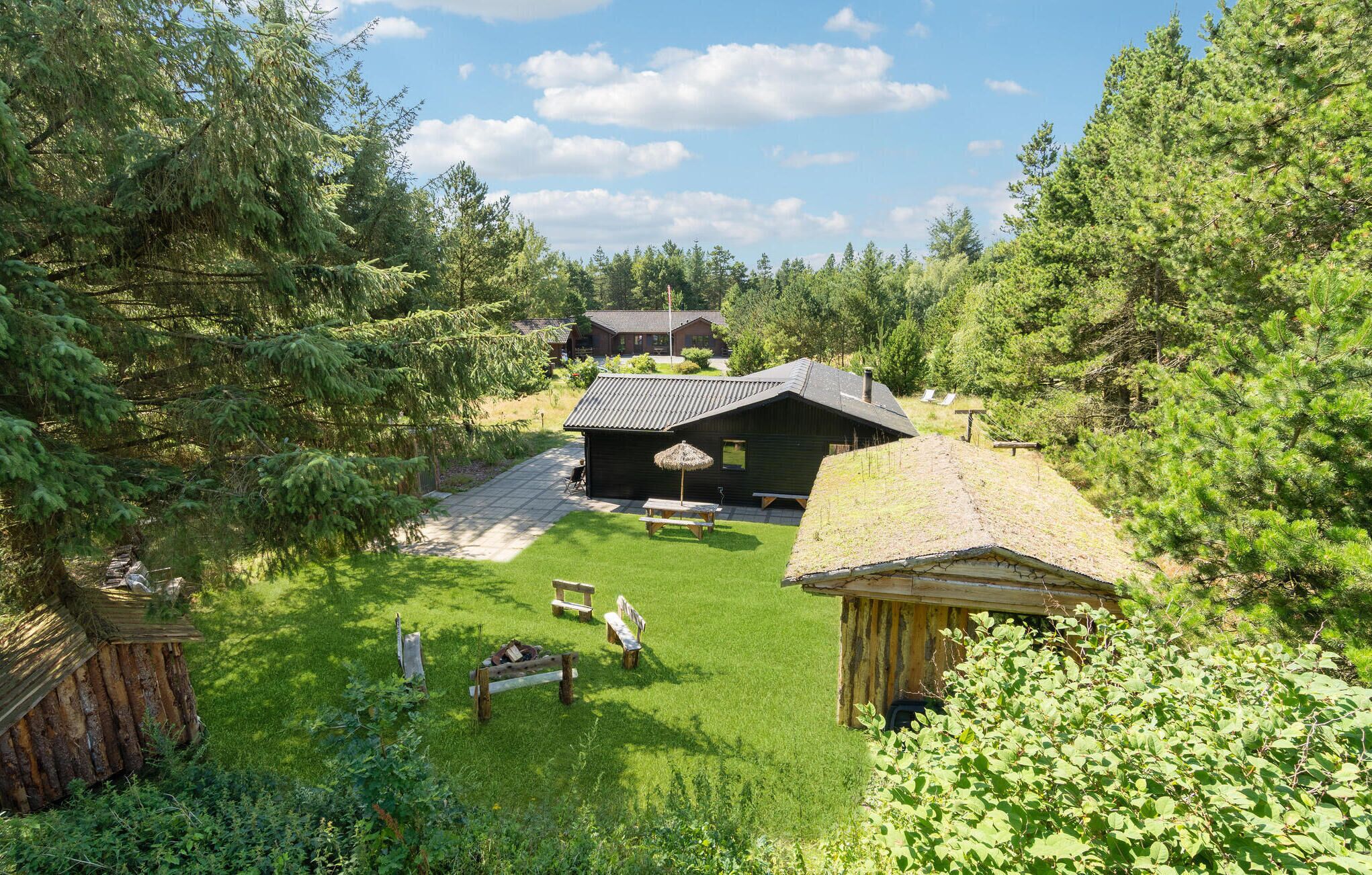 Una cabaña rústica con techo de paja y terraza de madera, rodeada de un bosque frondoso.