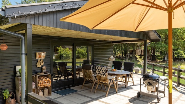 Ein überdachter Außenbereich mit Tisch, Stühlen und Grill.