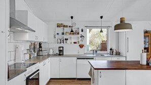 A modern kitchen with white cabinetry, a wooden countertop, a built-in oven, a dishwasher, and a window with a view of trees. - Stunning home in Ebeltoft with kitchen (Ebeltoft)