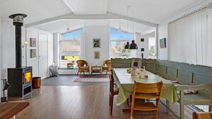 A spacious room with a high ceiling, a dining area with a long table and chairs, a sofa, and a wood-burning stove. - Stunning home in Ebeltoft with kitchen (Ebeltoft)