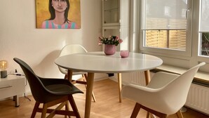 Un comedor con una mesa redonda, dos sillas, un florero con flores e iluminación colgante.