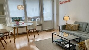 Una sala moderna con una mesa de centro de vidrio, un sofá gris y un comedor con una mesa y sillas blancas.