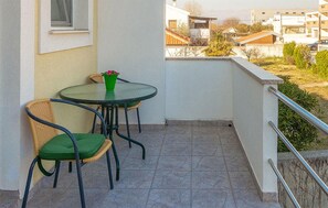 Ein kleiner Balkon mit Tisch und zwei Stühlen, ein Fenster und Blick auf eine Wohngegend.