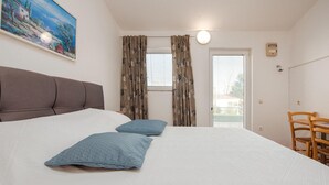 A bedroom with a large bed, two pillows, a headboard, a painting on the wall, curtains, a window, and a wooden chair. - StunNing apartment in Nin with WiFi (Nin)