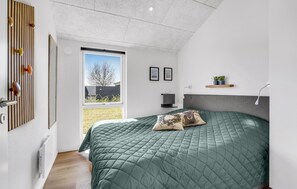 Ein modernes Schlafzimmer mit einem großen Bett, einem Fenster mit Blick ins Freie, einem Wandbild und einem kleinen Regal mit Pflanzen.