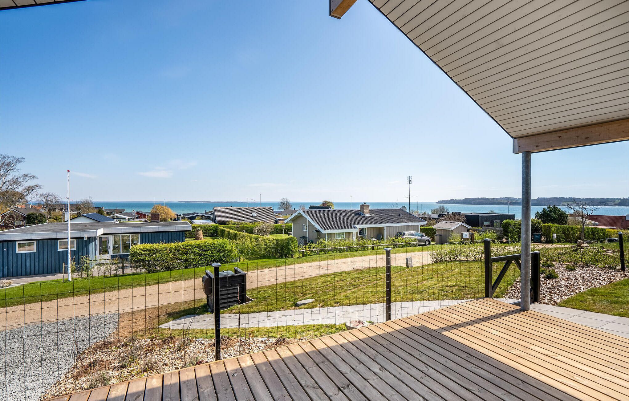 A residential area with a view of the sea, featuring houses with different architectural styles, a paved walkway, and a wooden deck.