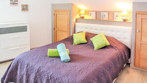 Une chambre à coucher bien rangée, avec un lit, deux tables de chevet, une armoire et une étagère murale agrémentée d’objets décoratifs.