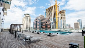 A rooftop pool area with lounge chairs and a pool, surrounded by modern buildings and a construction crane.