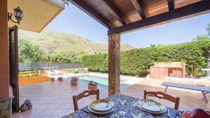Une terrasse avec une table dressée pour deux personnes, offrant une vue sur une piscine et un paysage montagneux.
