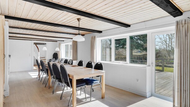 Een ruime eethoek met een houten tafel en stoelen, grote ramen en uitzicht op de omgeving.