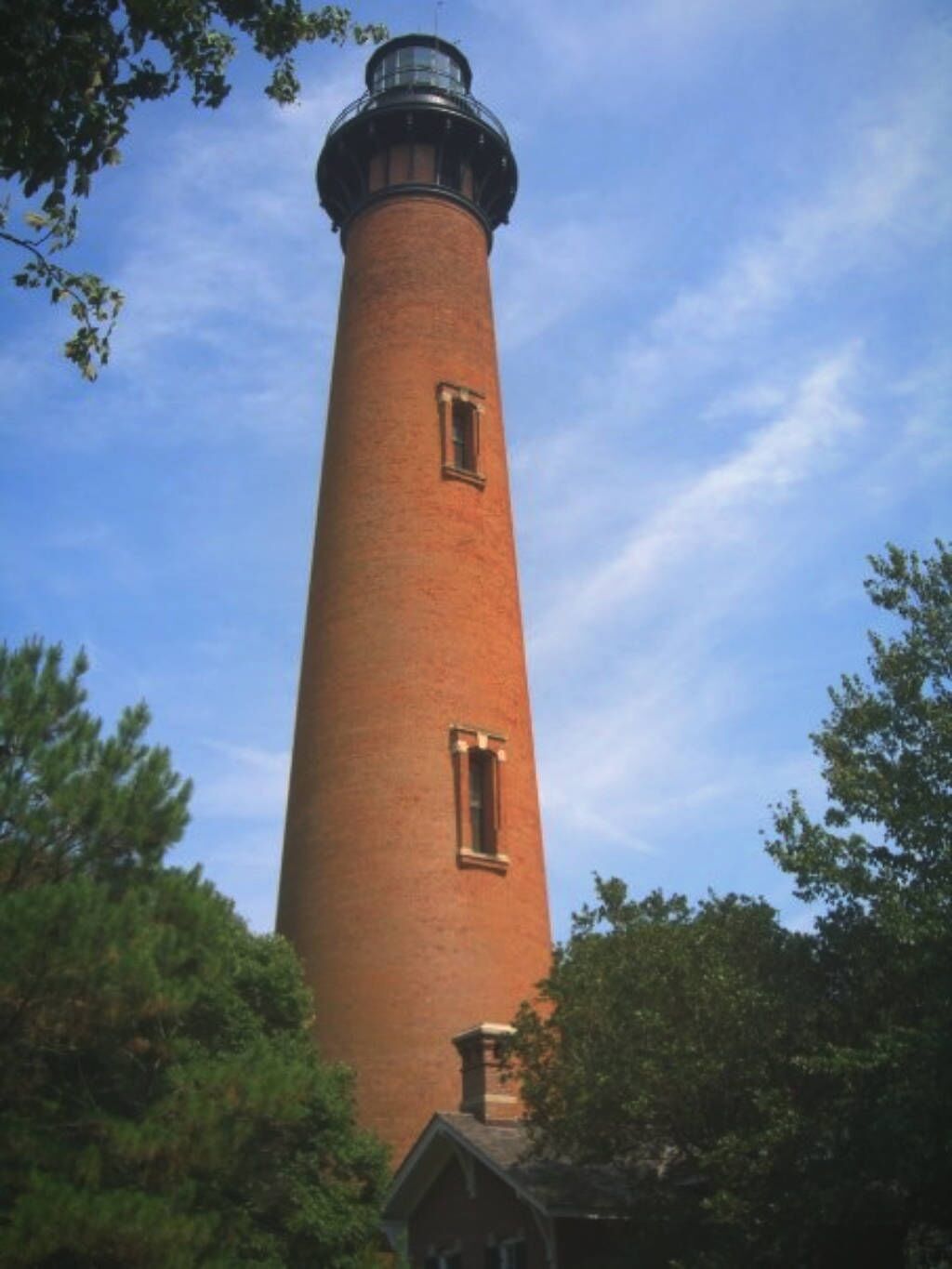 Un grand phare en briques, de forme cylindrique, doté d’une petite fenêtre et d’une lanterne au sommet.