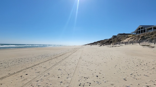 Una playa extensa de arena con huellas y cielo despejado.