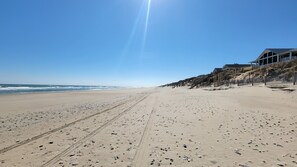 Ein weiter Sandstrand mit Fußspuren und blauem Himmel.