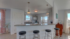 Una cocina con una isla central, taburetes de bar, lámparas colgantes y vistas a la ciudad.