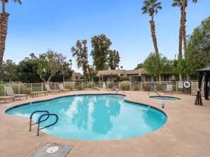 A swimming pool with a diving board, surrounded by palm trees and lounge chairs.