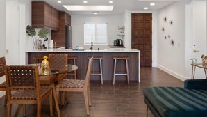 A modern kitchen with wooden cabinets, a central island with stools, and a dining area with chairs. - LUXURY mid century modern Palm Springs/Golf cart & bicycles/best view (Cathedral City)