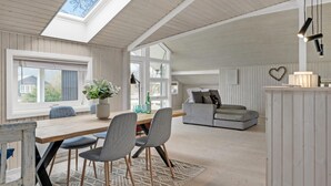 Une pièce spacieuse avec un plafond haut, une table à manger en bois avec des chaises, un canapé et un petit coin cuisine agrémenté d’une décoration en forme de cœur sur le mur.