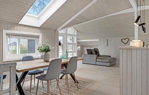Relax in this open-plan living space with a high ceiling and skylight, featuring a dining table, sofa, and cozy seating area.