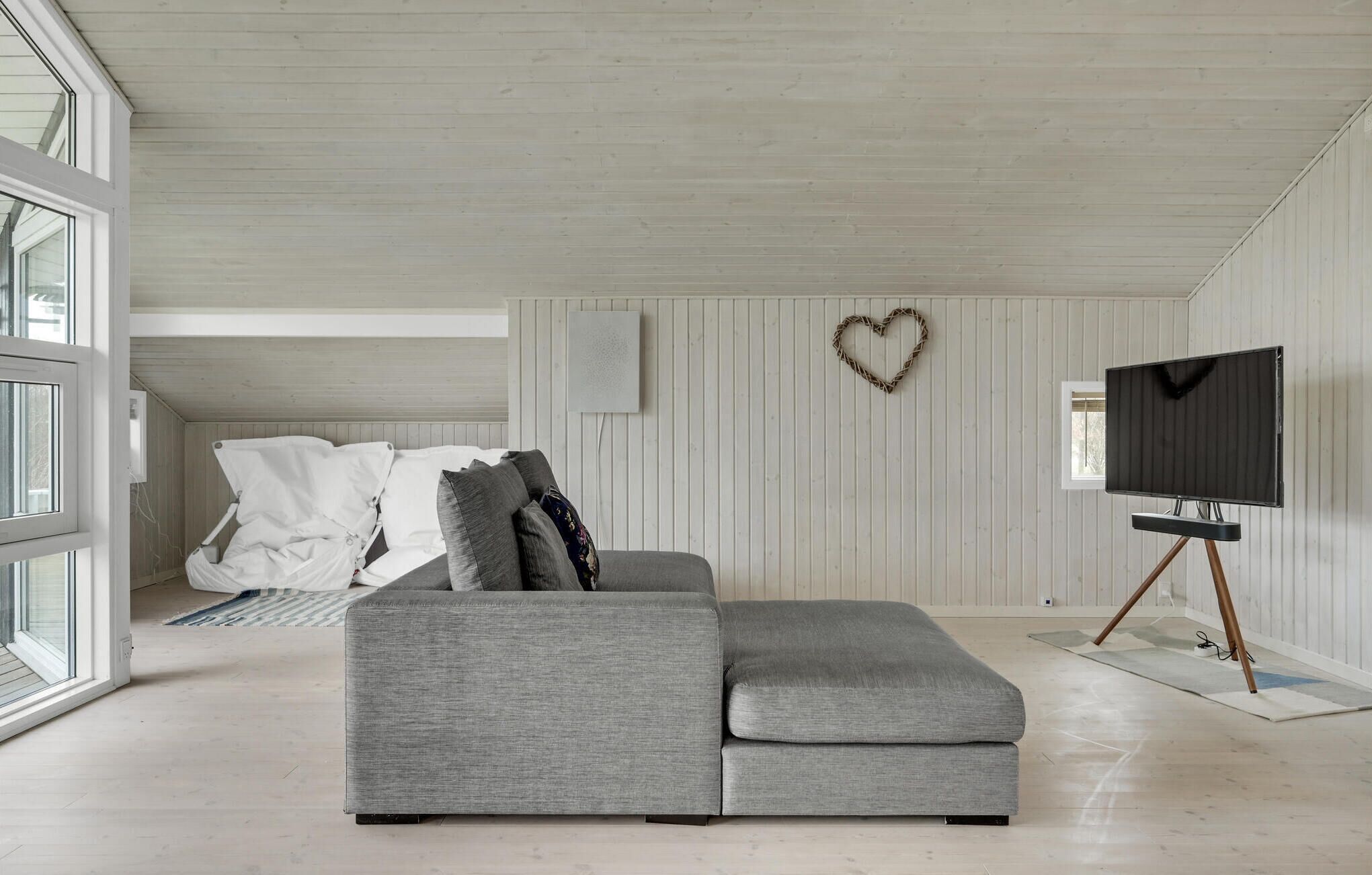 Una sala moderna con un sofá seccional gris, un televisor de pantalla plana sobre un mueble bajo y una decoración con forma de corazón en la pared.