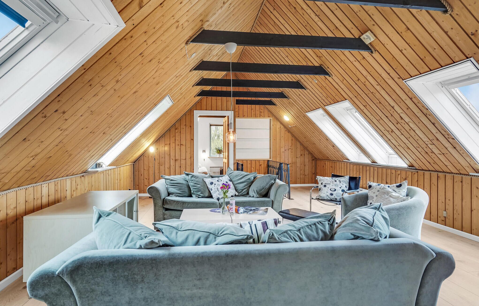 Une pièce mansardée chaleureuse, avec un plafond en pente, des poutres en bois et une grande fenêtre.