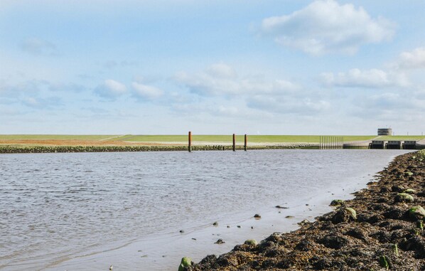 Eine Küstenlandschaft mit Sandstrand, ruhiger See und einem Gebäude mit flachem Dach in der Ferne.