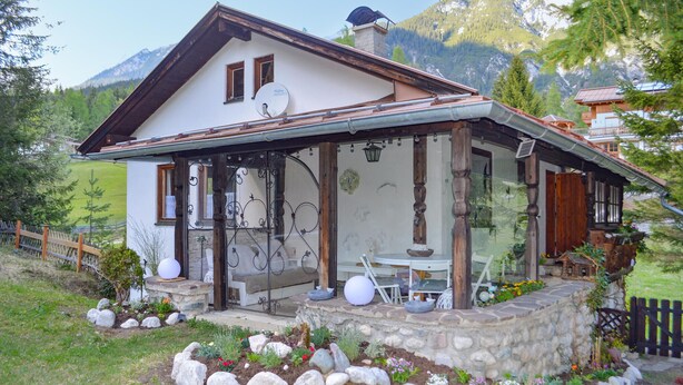 Un chalet avec des fondations en pierre, une véranda en bois et un coin repas doté de sièges extérieurs.