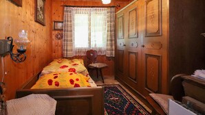 Une pièce chaleureuse aux murs en bois, avec un lit recouvert d’une literie à motifs floraux, une petite table, une chaise et un tapis à motifs.