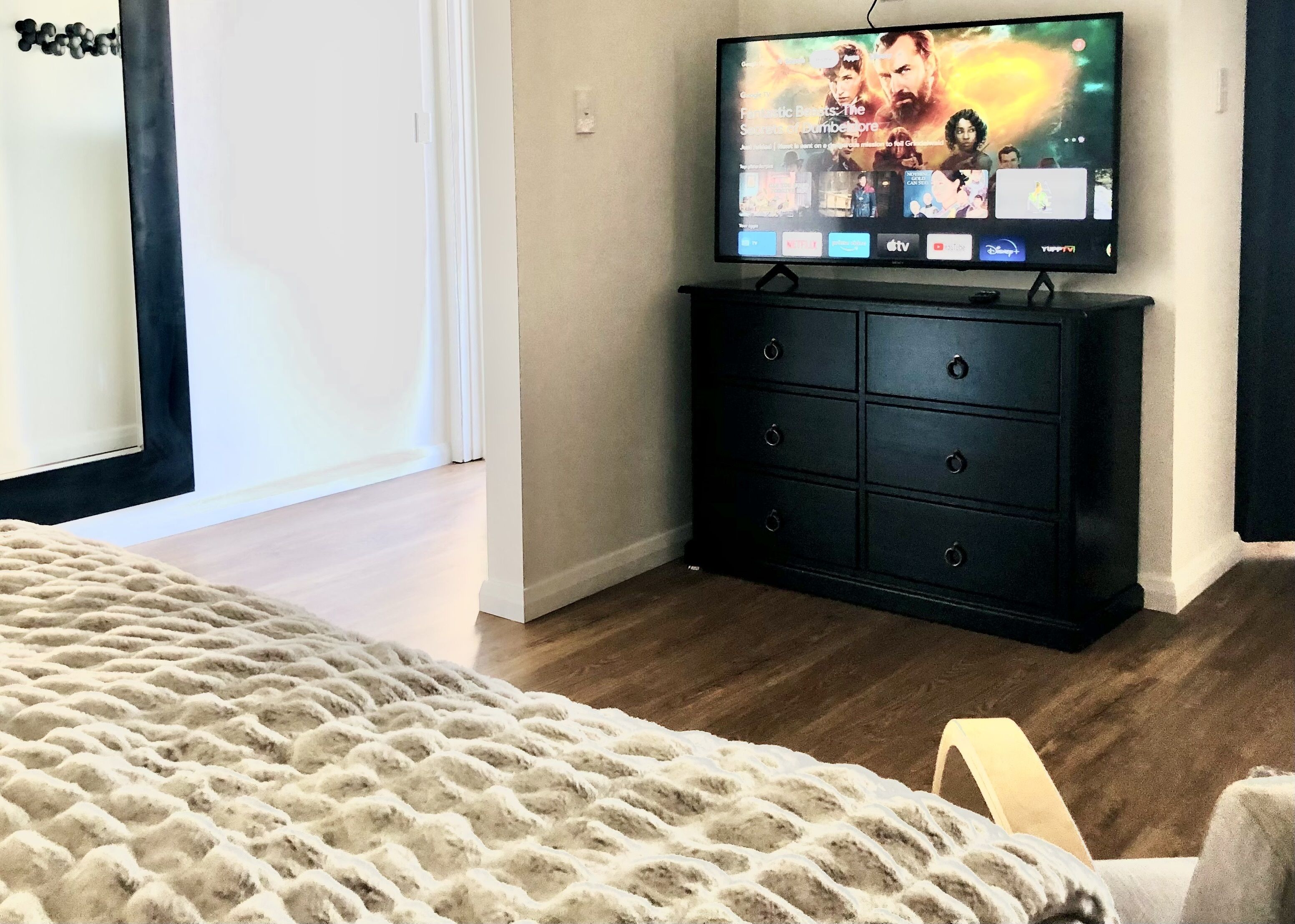 Quarto com cama, penteadeira e televisão exibindo um filme.