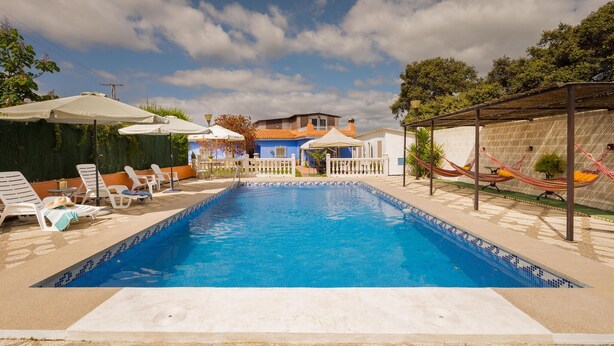 A swimming pool with lounge chairs and umbrellas, surrounded by a fence and trees. - Amazing home in Guillena (Guillena)