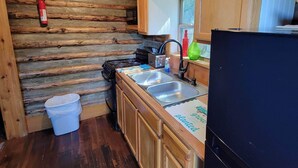 Une cuisine de taille réduite, avec des meubles de rangement en bois, un réfrigérateur noir et une fenêtre au-dessus de l’évier.