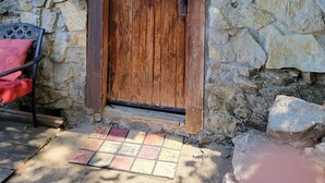 Une porte en bois, surmontée du chiffre « 5 », est encastrée dans un mur de pierre. À proximité, on trouve un banc de pierre et un coussin rouge.