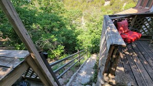 Une terrasse en bois avec un escalier en pierre menant à un espace salon agrémenté de coussins rouges, le tout entouré d’une végétation luxuriante.
