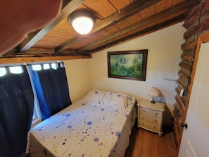 Une chambre à coucher avec un lit, une table de chevet, une lampe, un tableau et une fenêtre avec des rideaux.