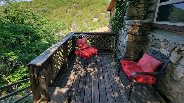 Une terrasse en bois avec deux chaises rouges dotées de coussins, un mur en pierre et une vue sur une colline boisée.