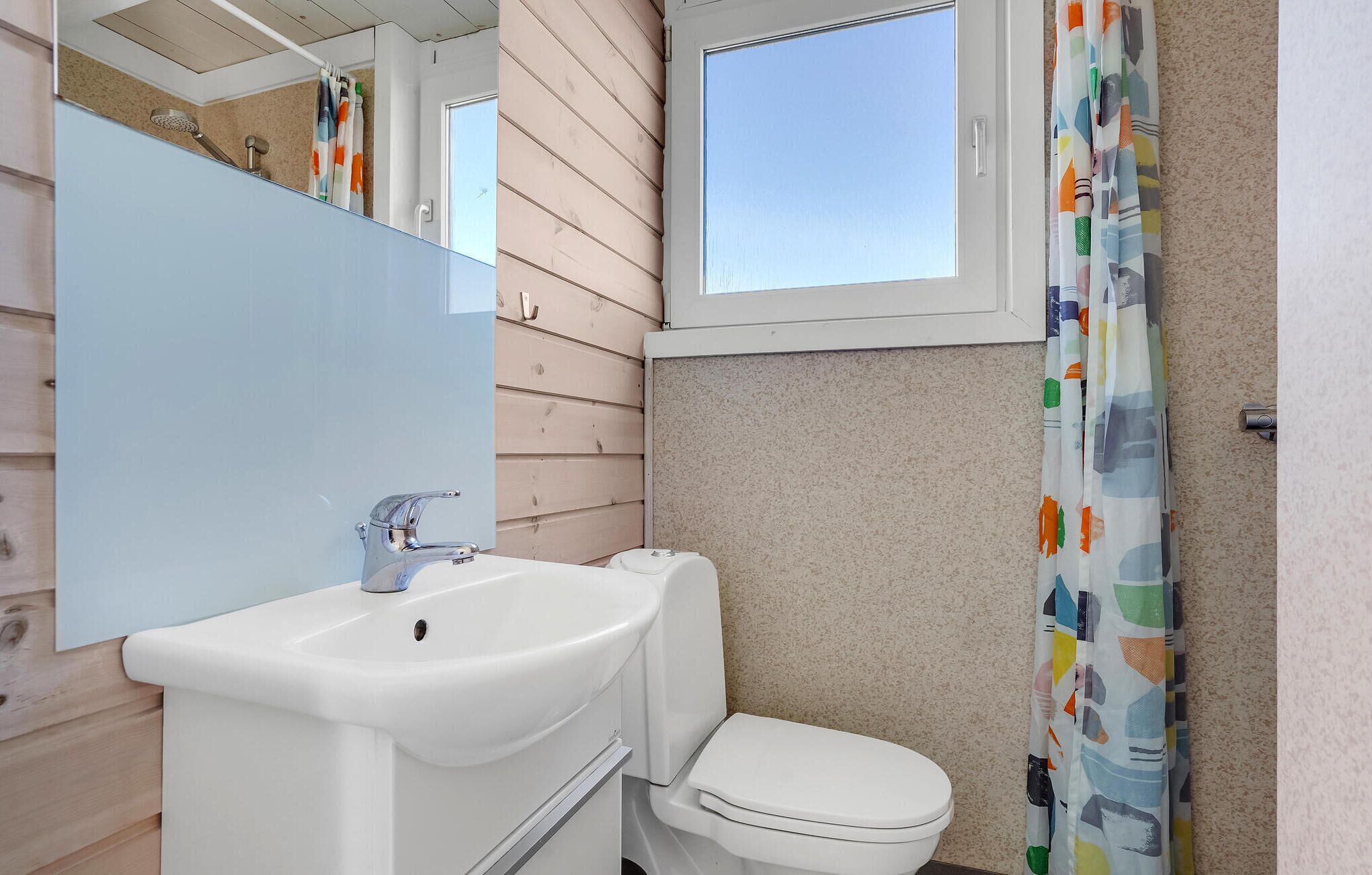 Une salle de bain avec un lavabo blanc, des toilettes et une fenêtre située au-dessus des toilettes.