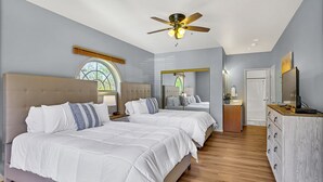 Un dormitorio con dos camas, ventilador de techo, espejo grande y cómoda de madera.