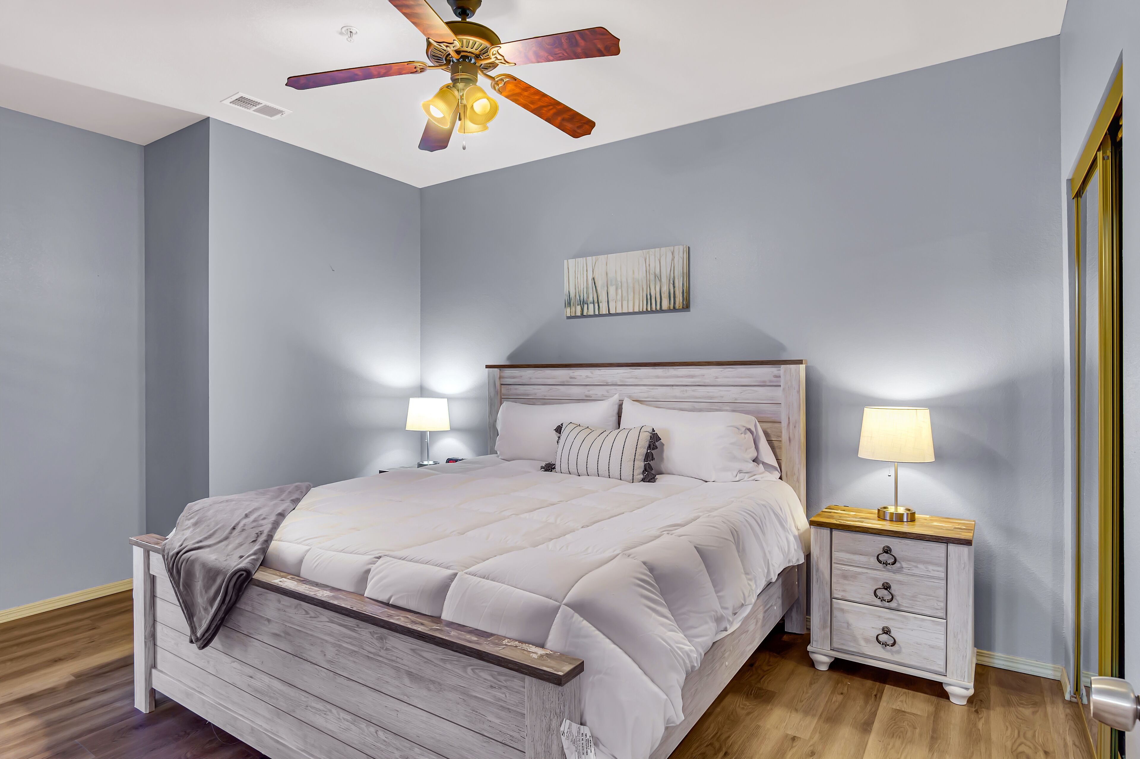 A bedroom with a bed, nightstands, a ceiling fan, and a wall-mounted artwork.