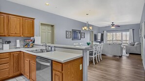 Una cocina moderna con armarios de madera, una isla central y una zona de comedor con sofá gris y sillas blancas.